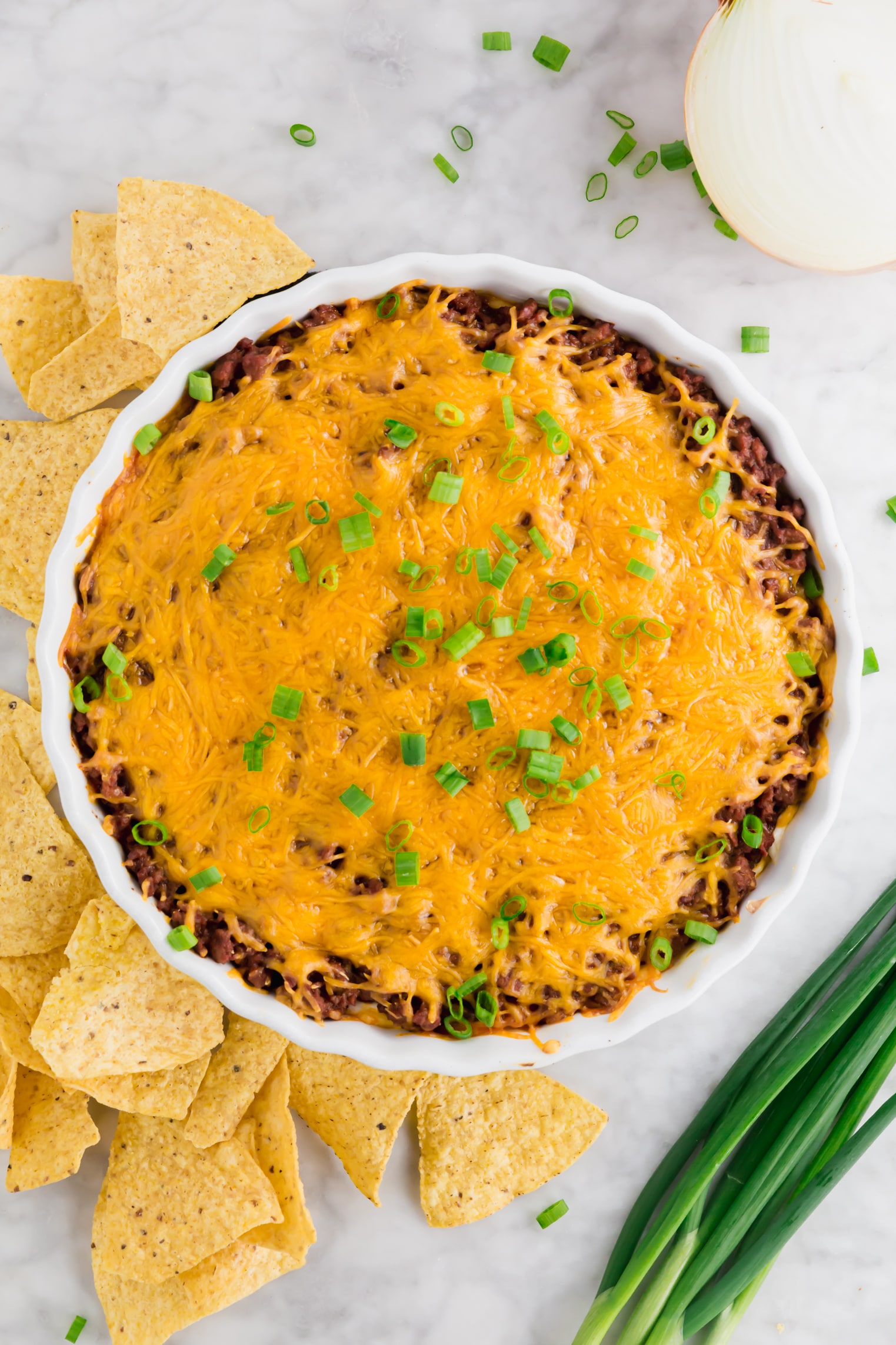 A photo of a tart pan filled with chili cheese dip topped with green onions.