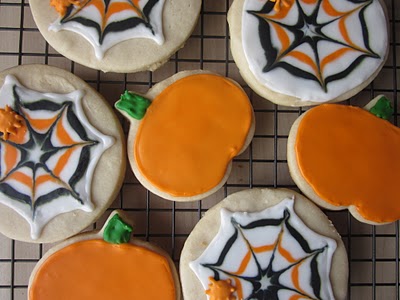 A cooling rack with orange and black spider web and pumpkin decorated sugar cookies.