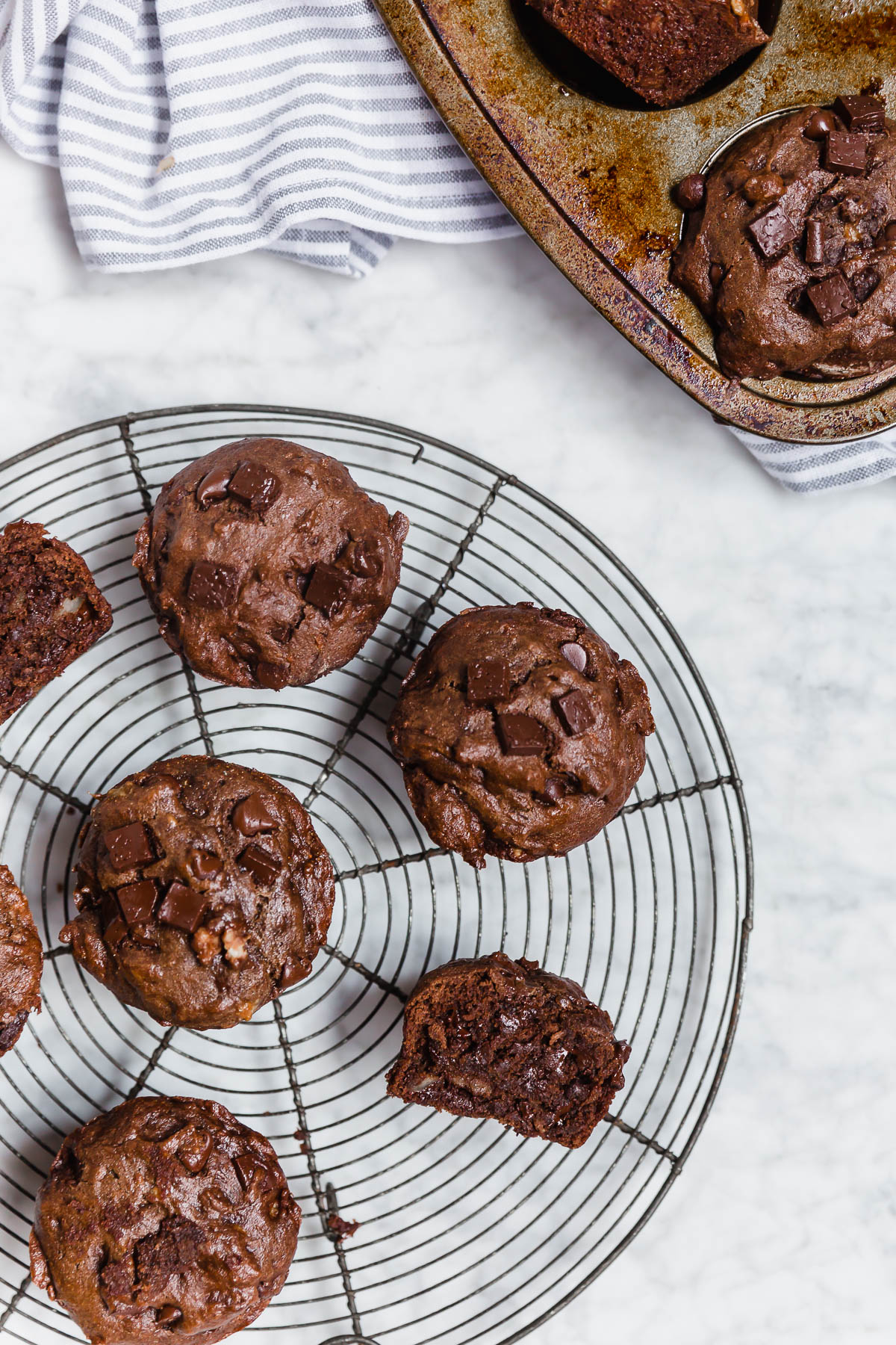 A round baking rack with gluten-free double chocolate chunk banana muffins on a white marble table.