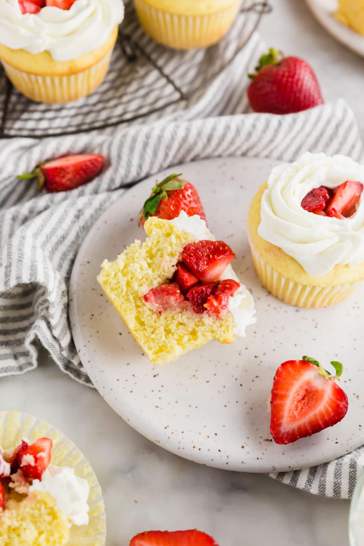Strawberry shortcake cupcakes on a plate with one sliced in half and fresh strawberries surrounding the plate.