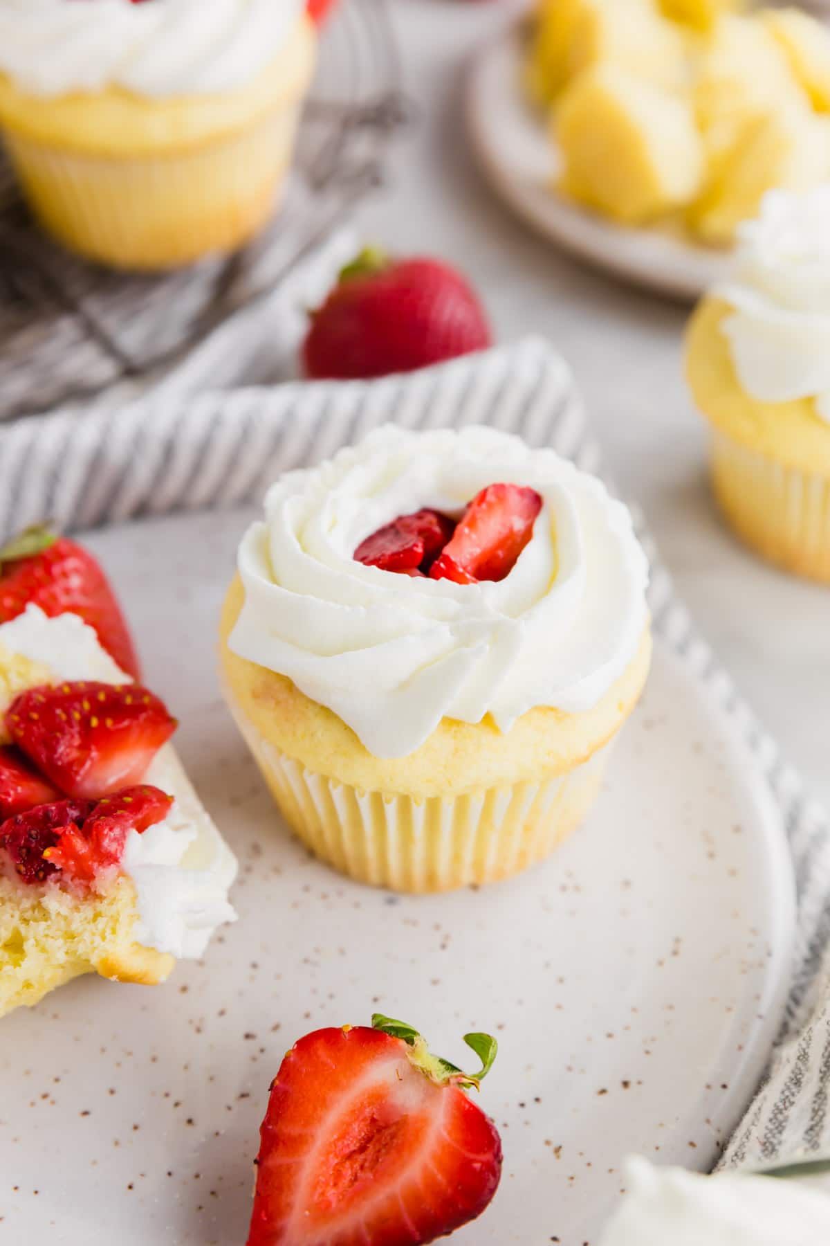 A photo of a strawberry shortcake cupcake topped with fresh whipped cream on a plate.