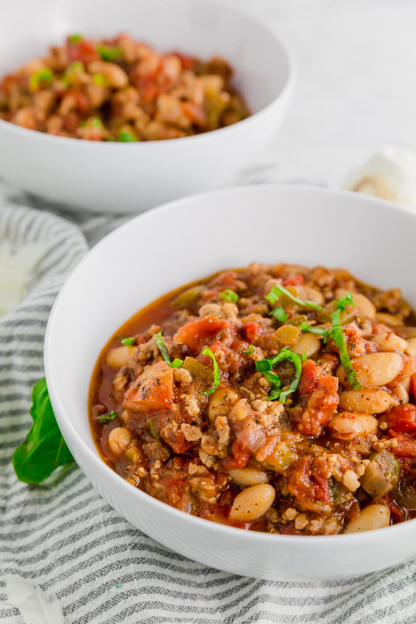 A photo of two bowls of italian sausage stew with white beans topped with fresh basil.