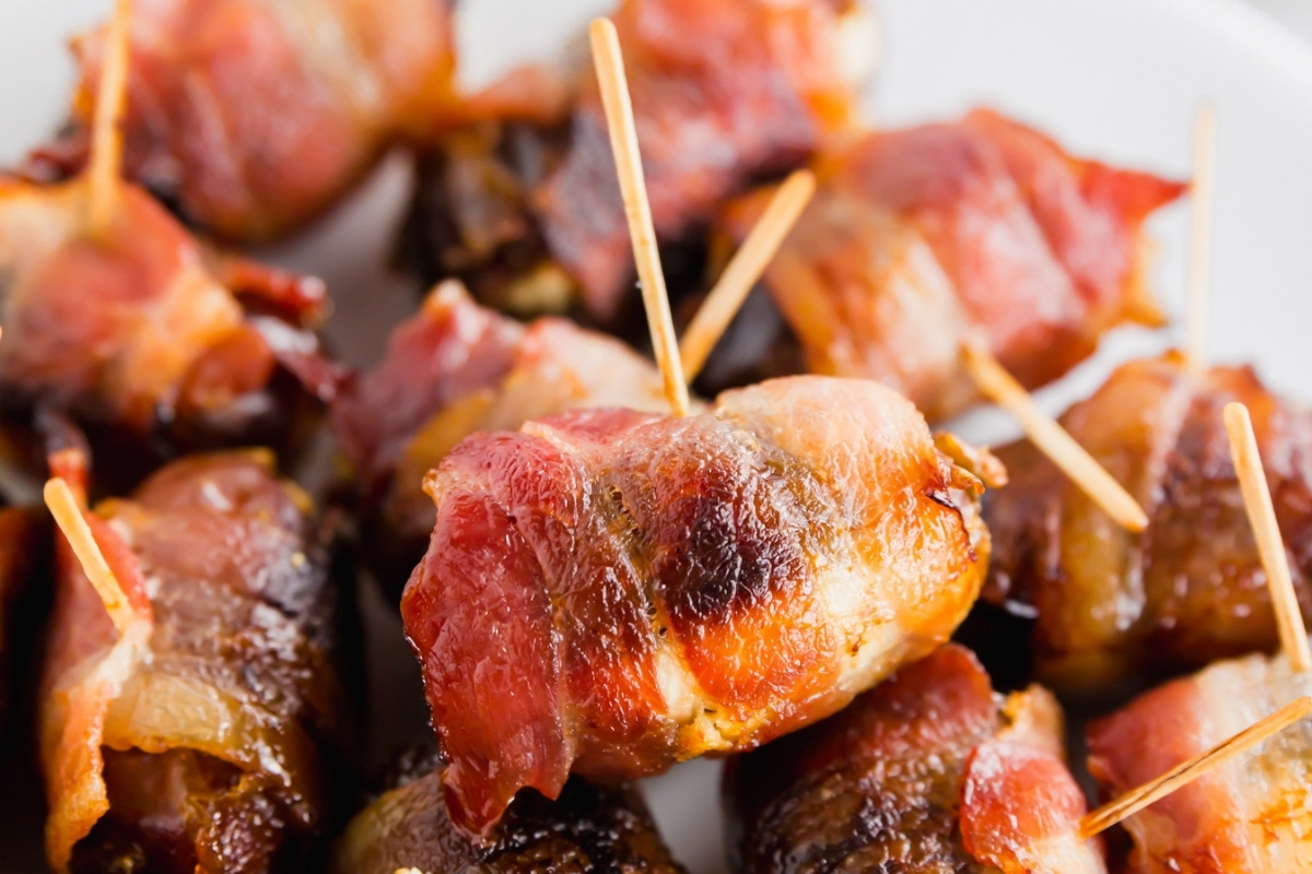 Close-up of bacon wrapped dates with goat cheese and toothpicks on a serving platter showing crispy bacon.