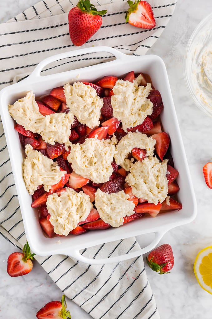 A photo of a baking sheet with strawberry cobbler topped with gluten free vegan biscuit dough ready to go in the oven and fresh strawberries.