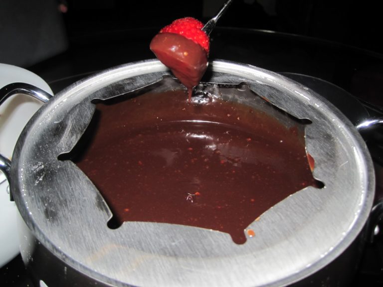 A strawberry on a fork is dipped in a pot of melted chocolate fondue, with the pots metal rim visible.