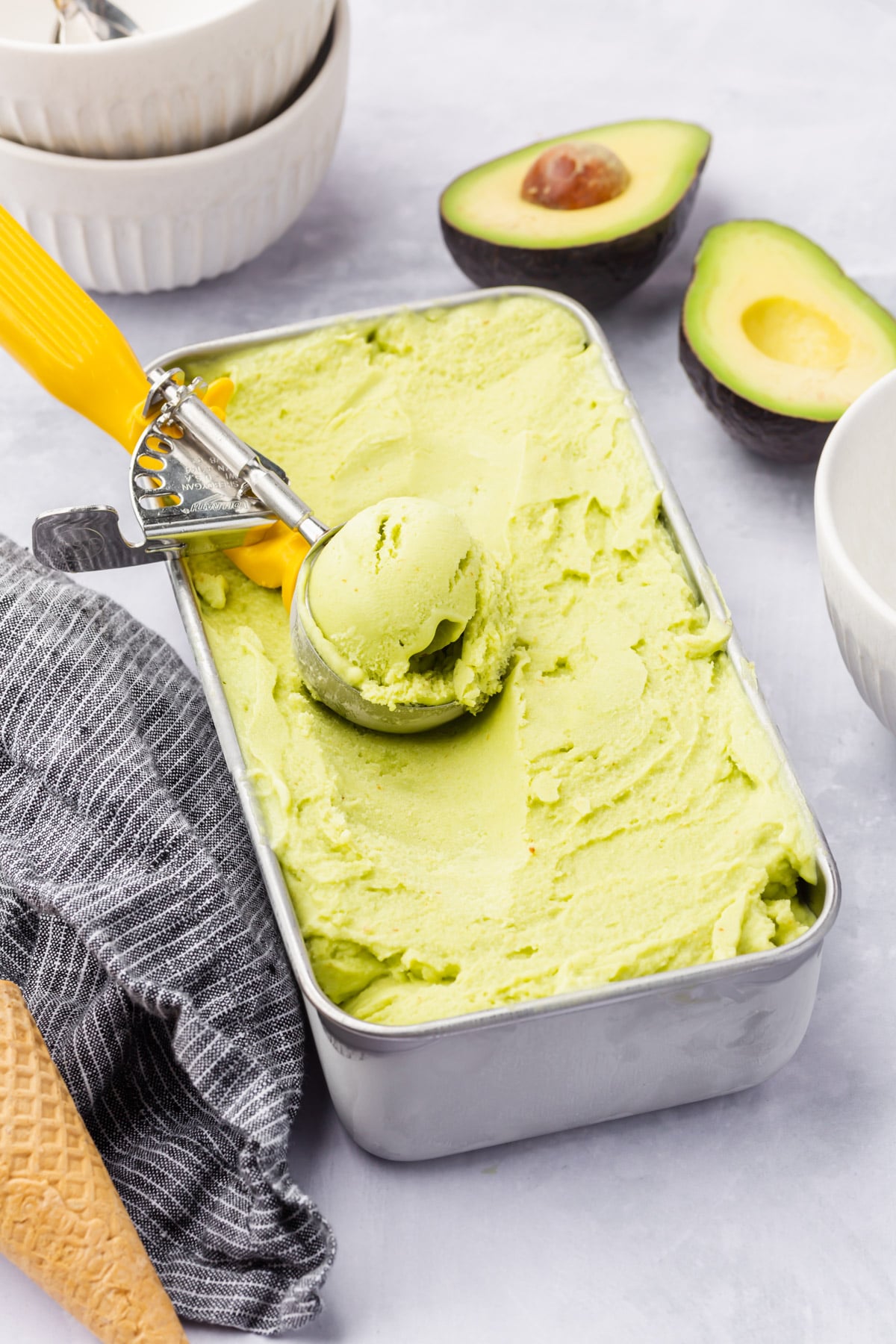 A loaf pan of avocado ice cream with a scooper in it.