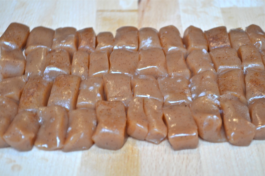 Rows of shiny, soft, brown caramel candy pieces arranged closely together on a light wooden surface.
