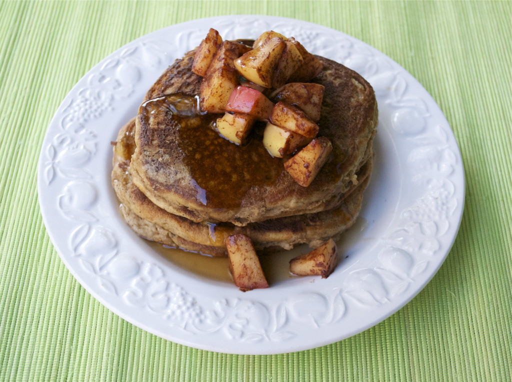 A stack of pancakes topped with sautéed apples and maple syrup.