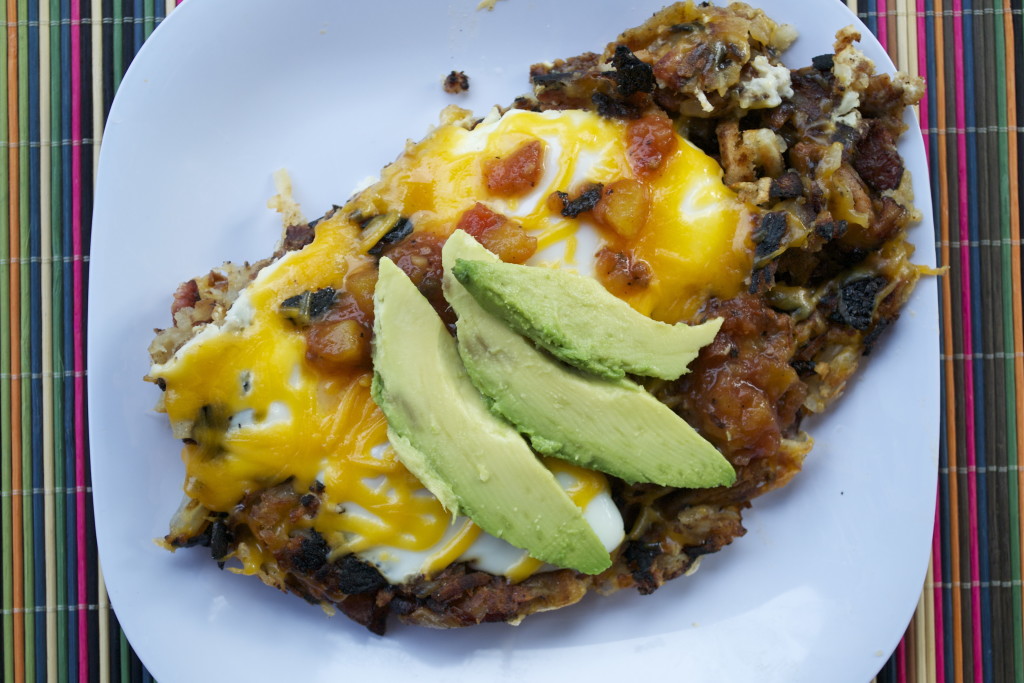 Hash Brown Egg Skillet topped with melted cheddar cheese, salsa and sliced avocado.