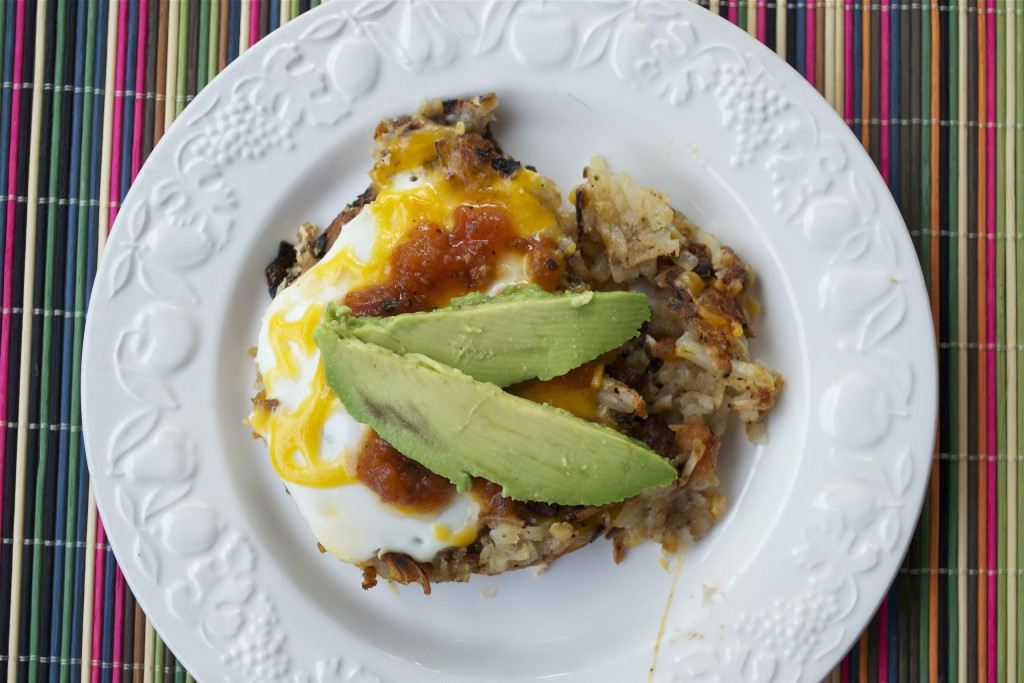 Hash browns topped with eggs, melted cheese, salsa, and sliced avocado.