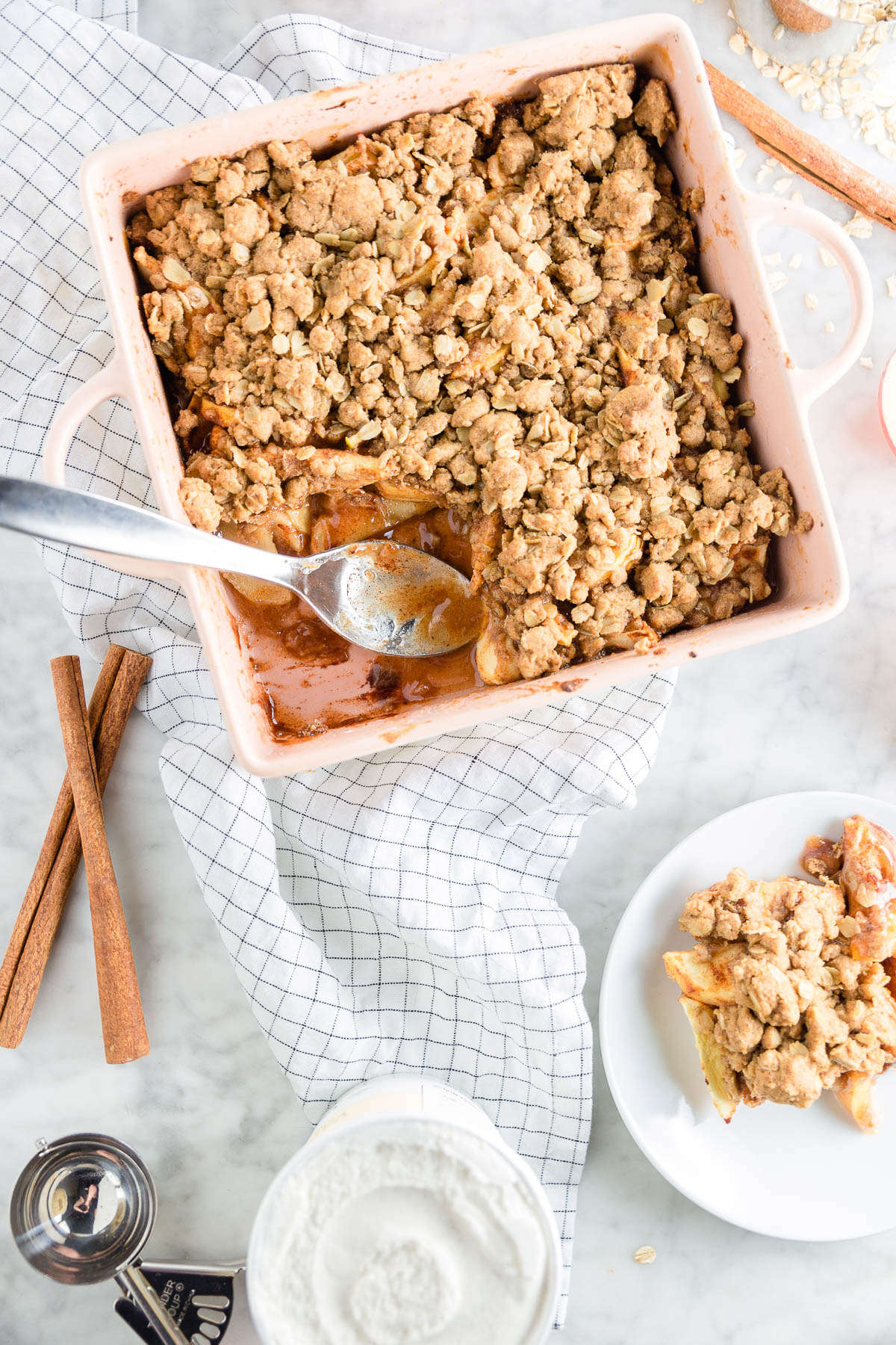 A square baking dish with gluten-free apple crisp and a plate with a big scoop.