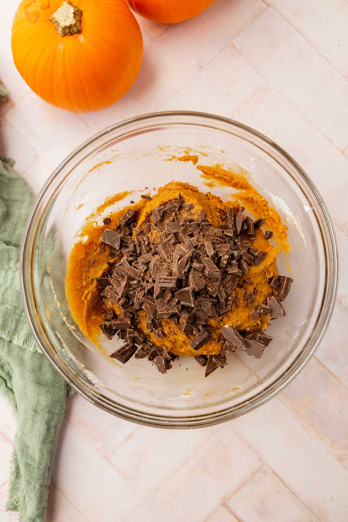 A glass mixing bowl with gluten-free pumpkin cookie dough topped with chopped chocolate chunks.