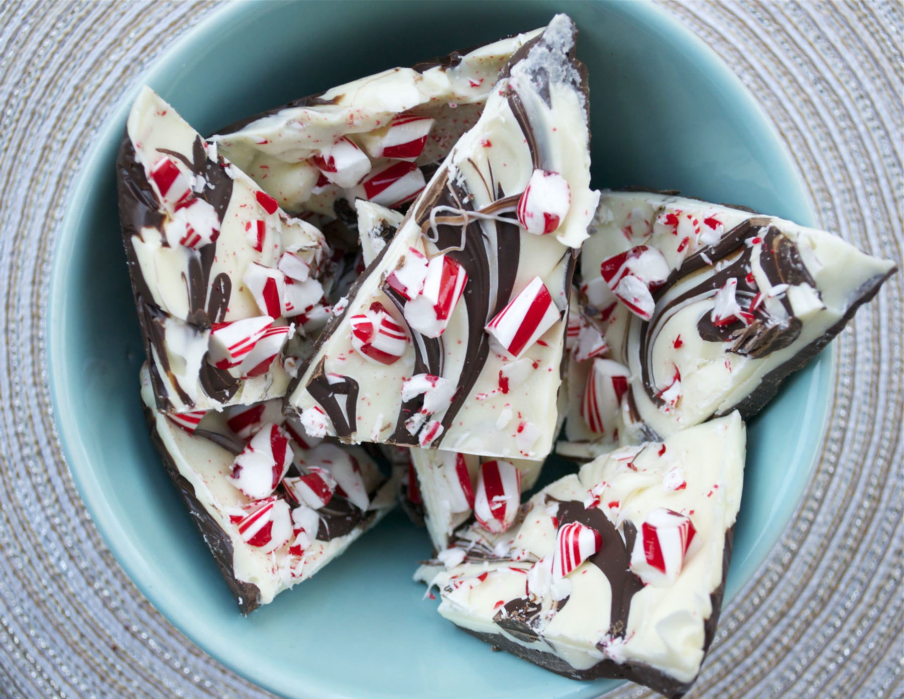 Broken pieces of chocolate peppermint bark with swirled dark and white chocolate and crushed candy canes in a teal bowl.