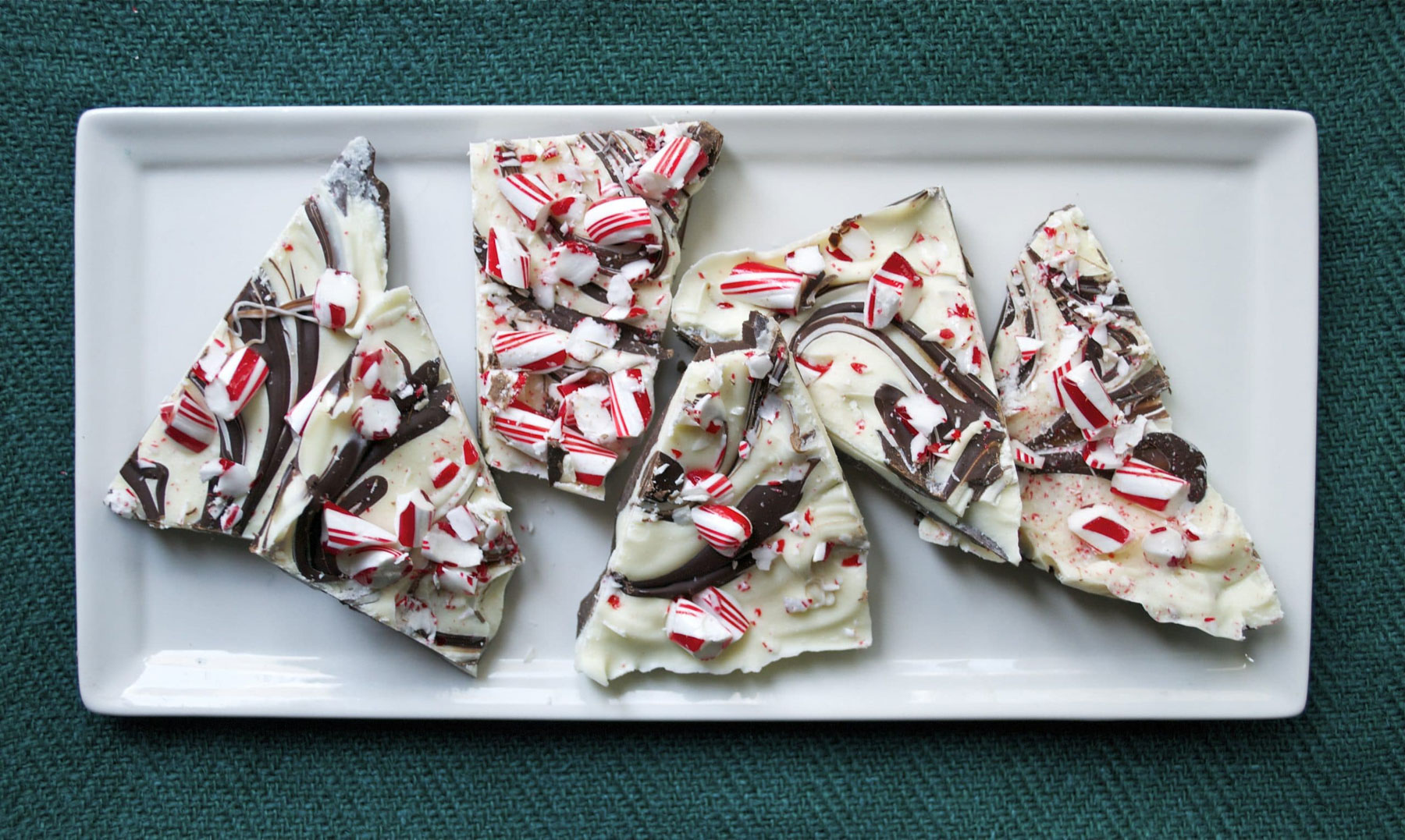 Chocolate peppermint bark pieces arranged on a white rectangular platter showing marbled chocolate swirls and candy cane topping.