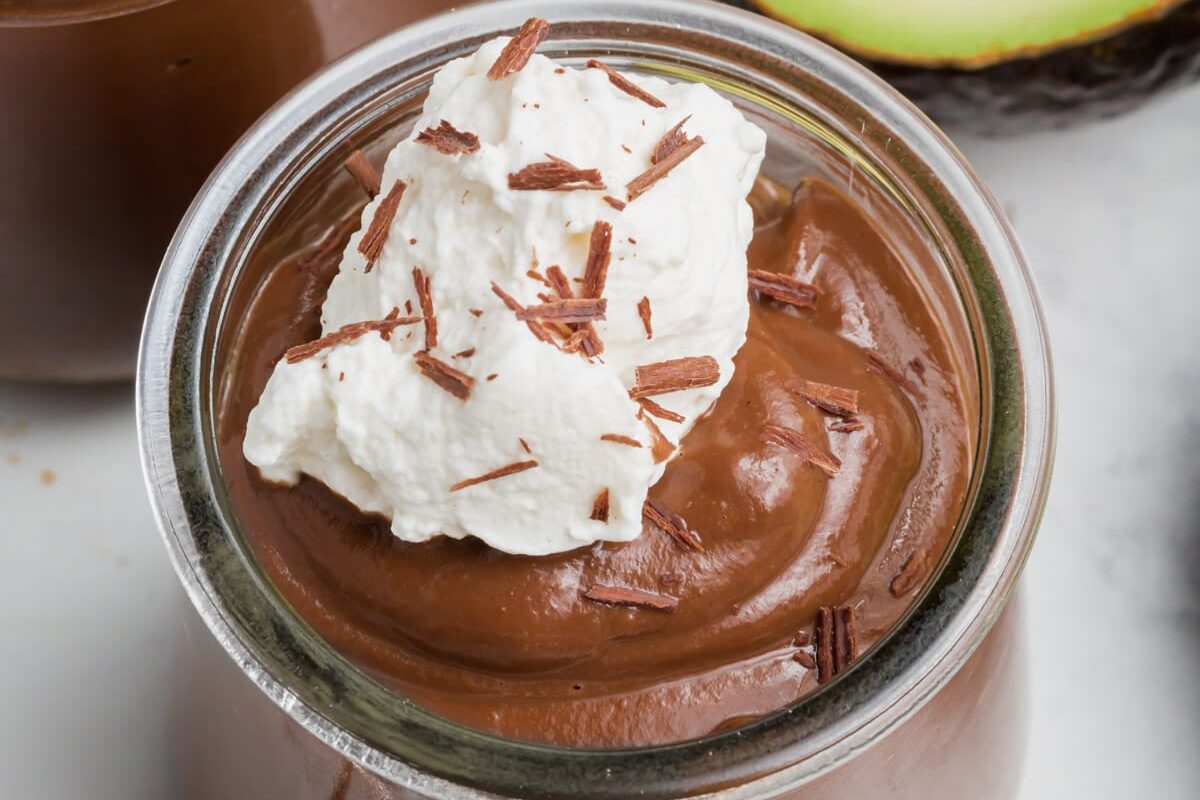 A glass jar filled with creamy chocolate avocado pudding, topped with a dollop of whipped cream and chocolate shavings.