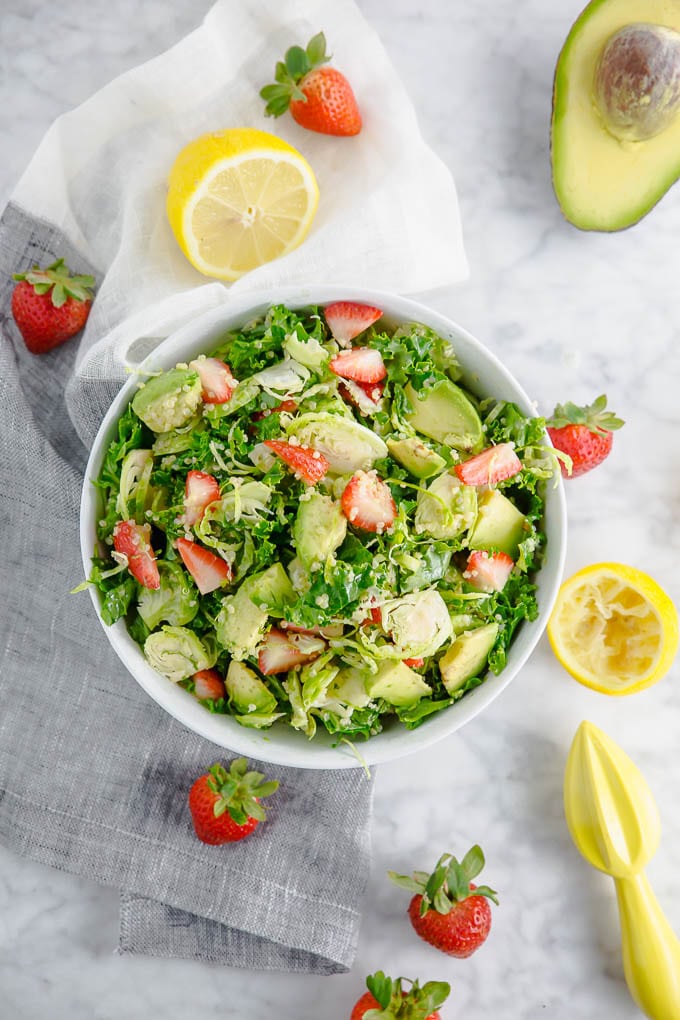 A bowl of brussels sprouts kale salad with strawberries and lemon.