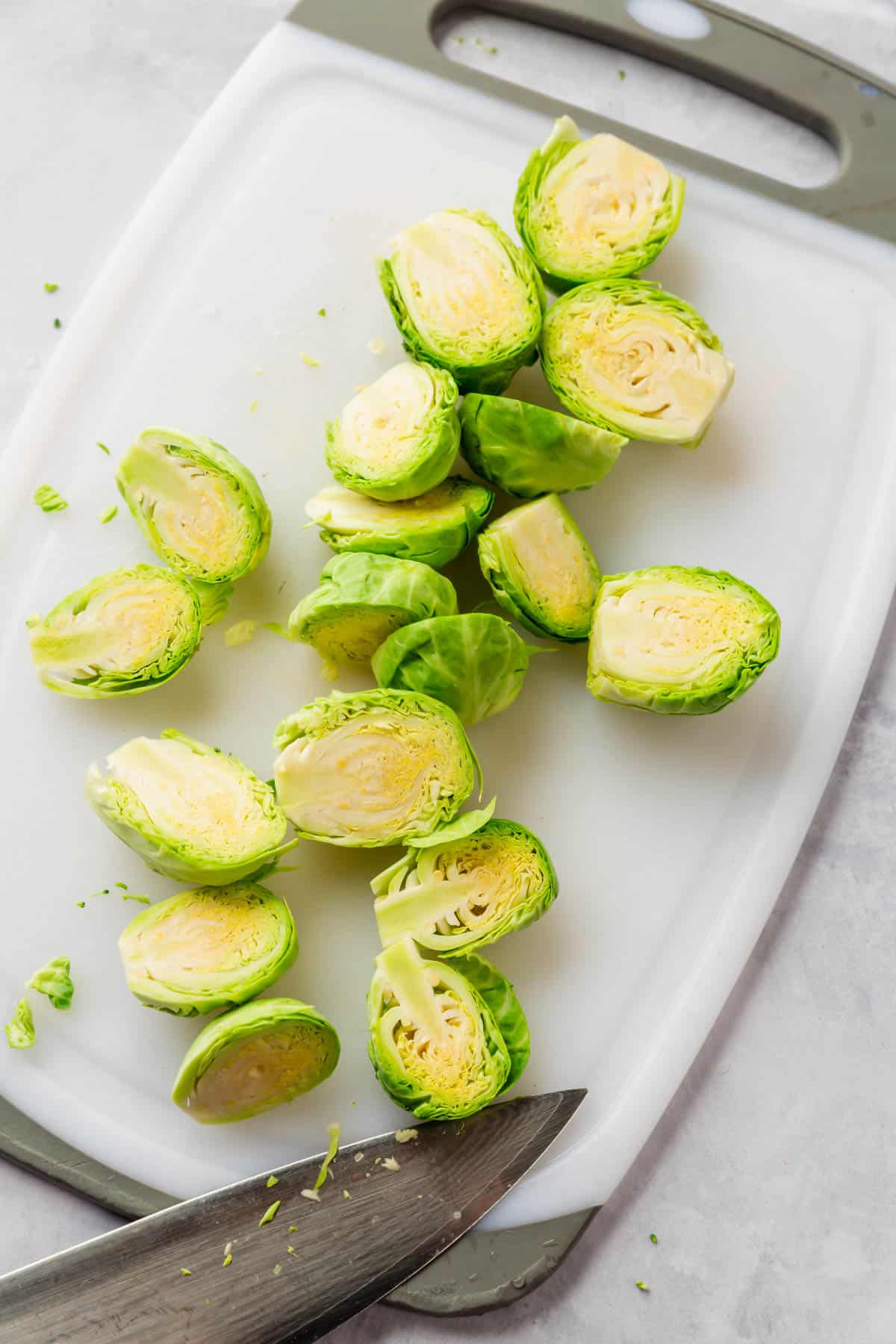Brussels sprouts trimmed and sliced in half on a white cutting board.