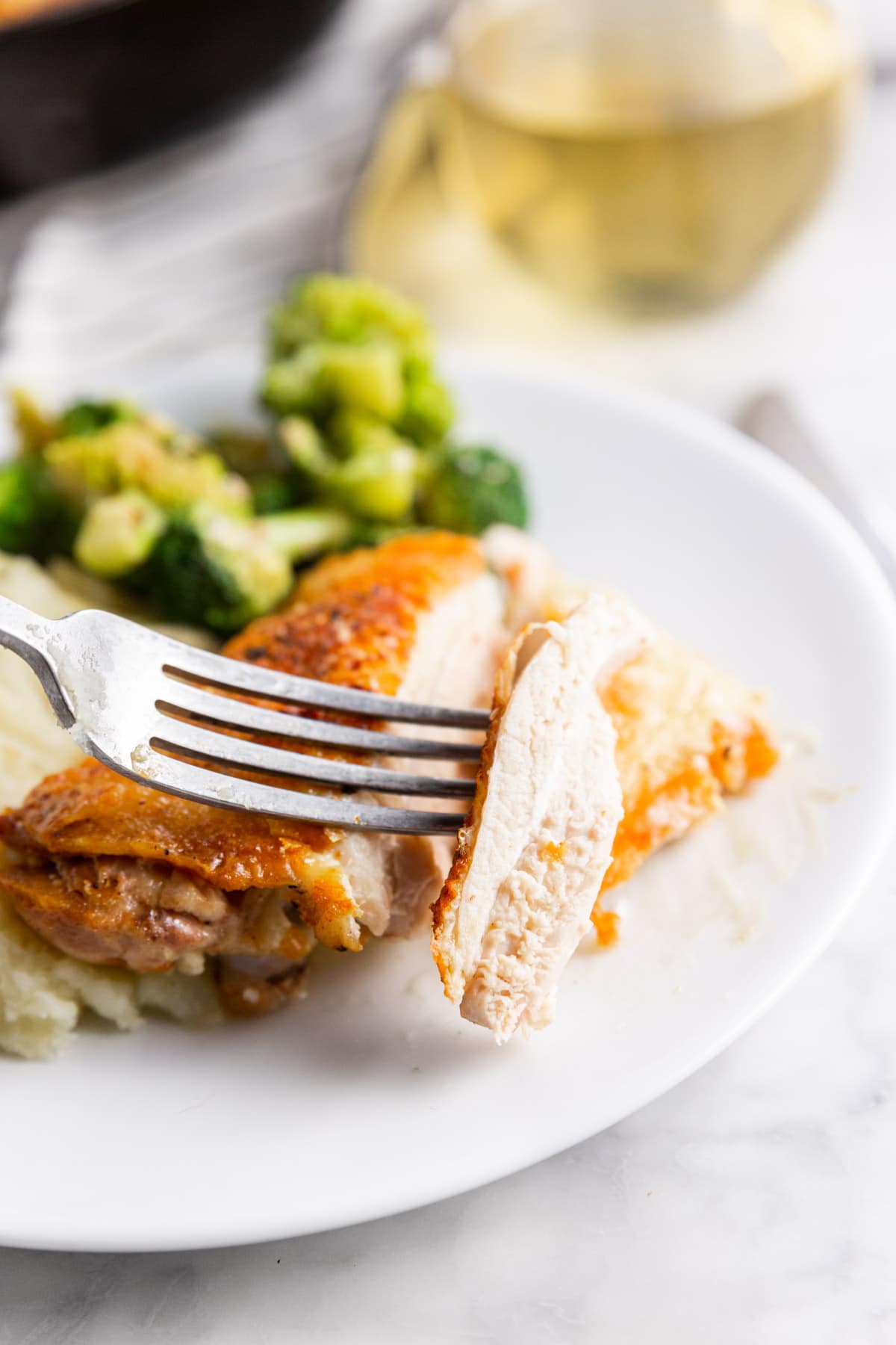 A plate with roasted chicken thighs with broccoli and mashed potatoes and a fork holding a slice of chicken.