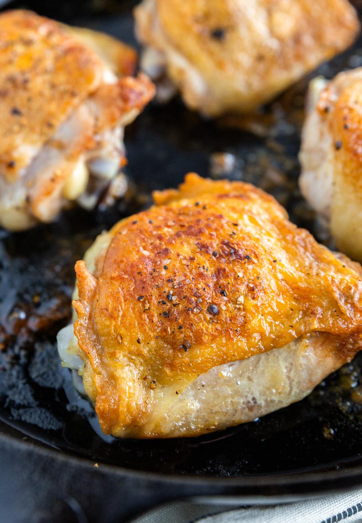 A photo of a cast iron skillet with crispy roasted chicken thighs topped with salt and pepper in it.