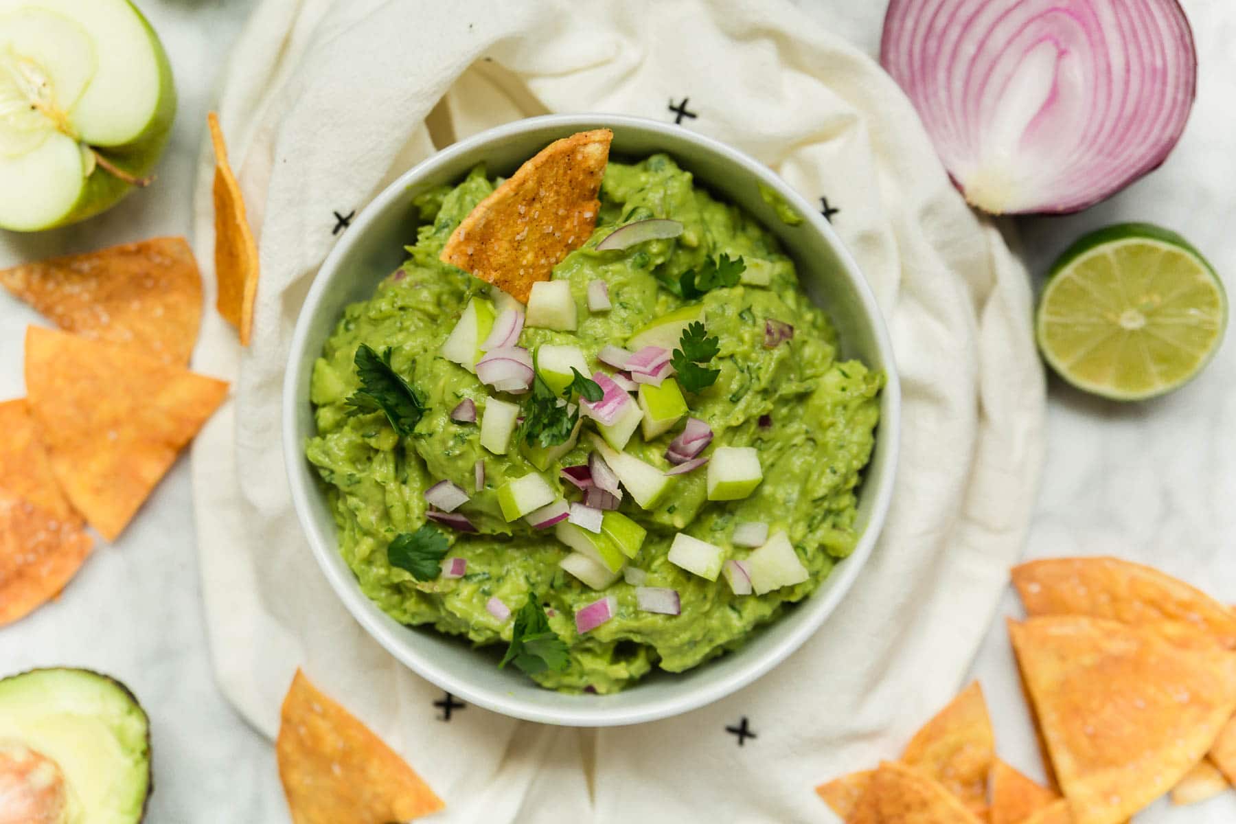 A bowl of apple guacamole with red onion, tortilla chips and lime.