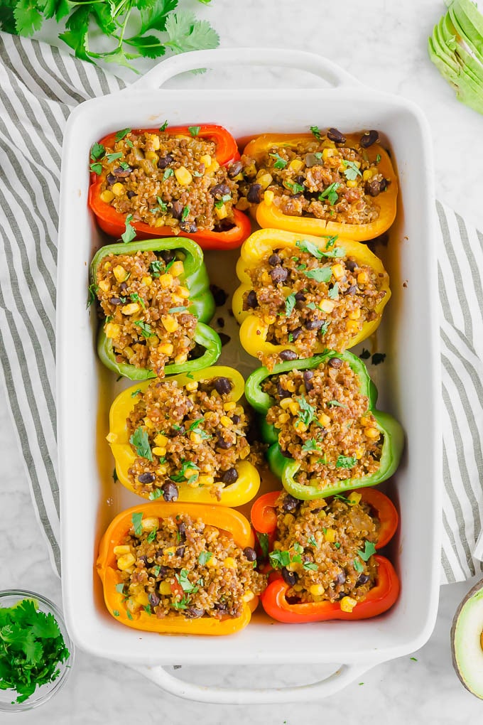 A large baking dish filled with colorful stuffed bell peppers with quinoa, beef, corn, and fresh cilantro.