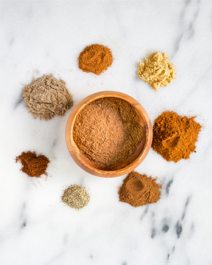 A small bowl of chai spice mix surrounded by individual spices used to make it.