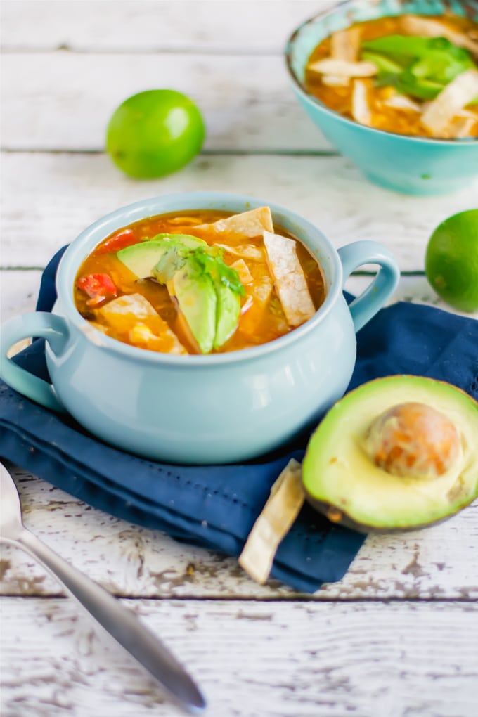 A crock of chicken tortilla soup topped with avocado and cilantro.