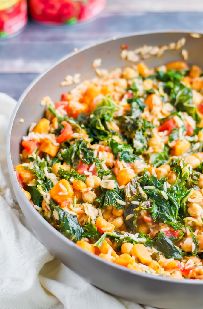 A close-up of a pan filled with a colorful One Pot Sweet Potato Skillet, featuring kale, chickpeas, tomatoes, yellow bell peppers, and rice all mixed together and cooked.