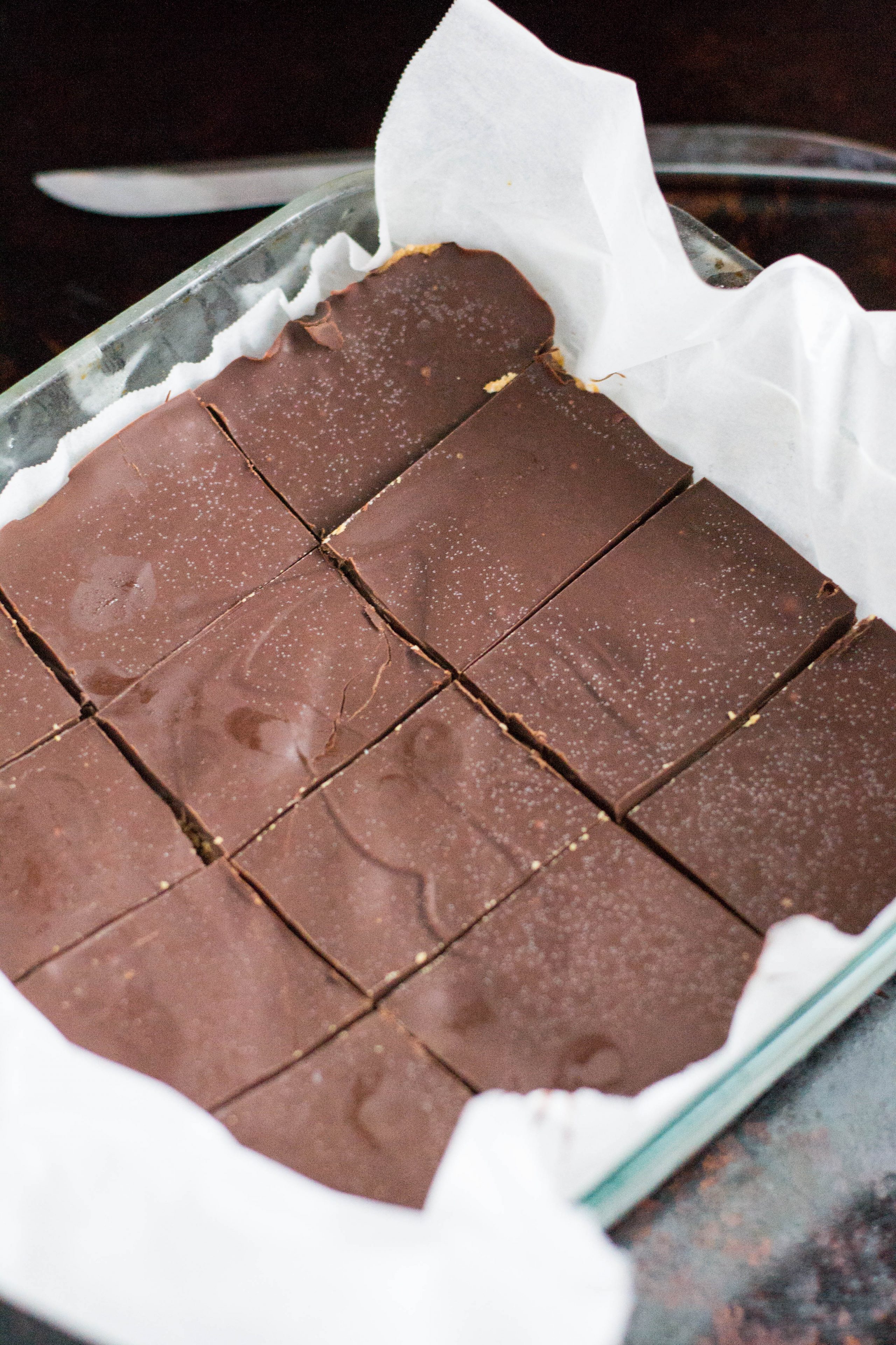 A baking dish lined with parchment paper containing chocolate peanut butter bars that have been sliced into rectangles.