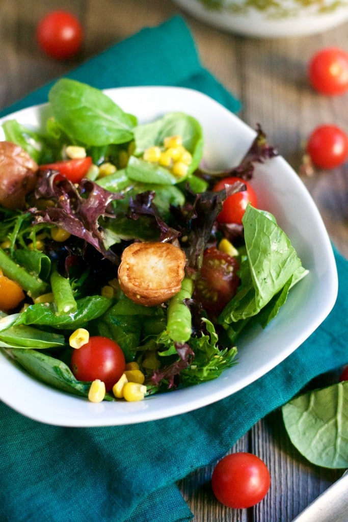 A bowl of salad with corn, cherry tomatoes, green beans, and roasted potatoes.