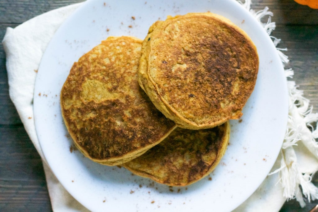 A plate of three pumpkin pancakes sprinkled with ground cinnamon.