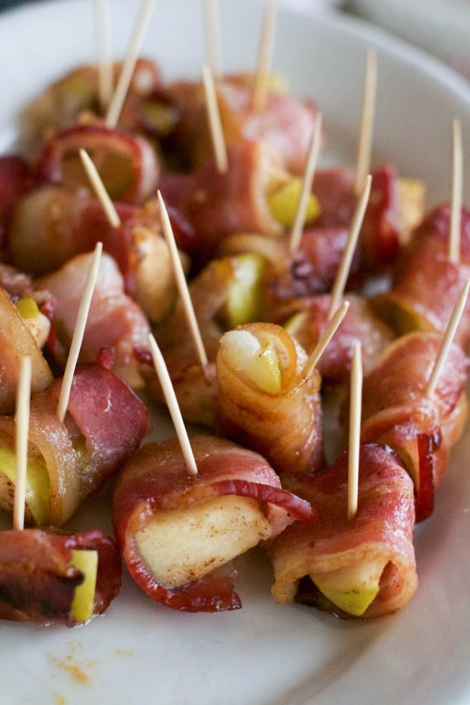 A platter of bacon wrapped apple bites with toothpicks sticking out of them.