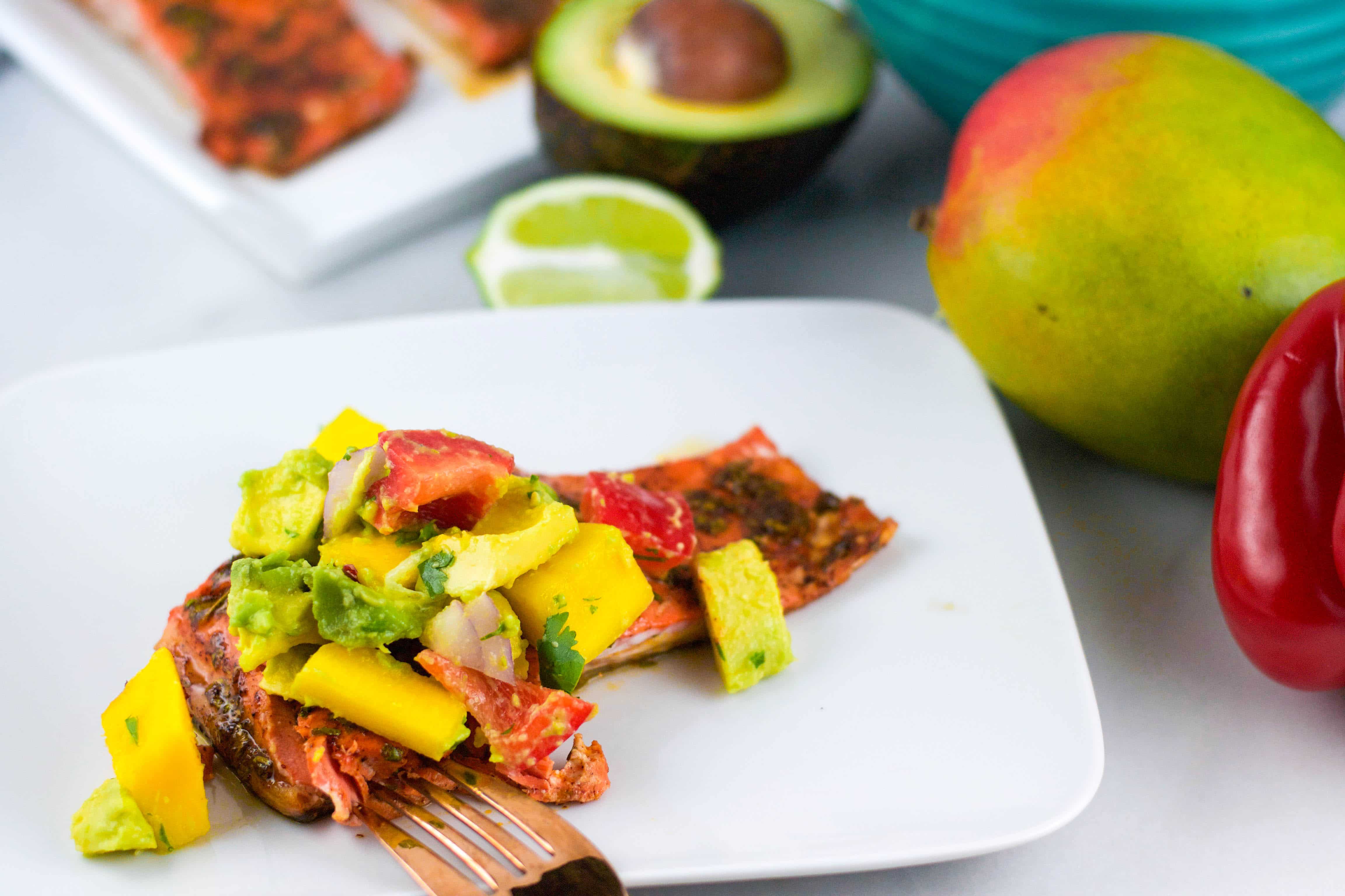 A plate of salmon with avocado mango salsa on top with a fork.