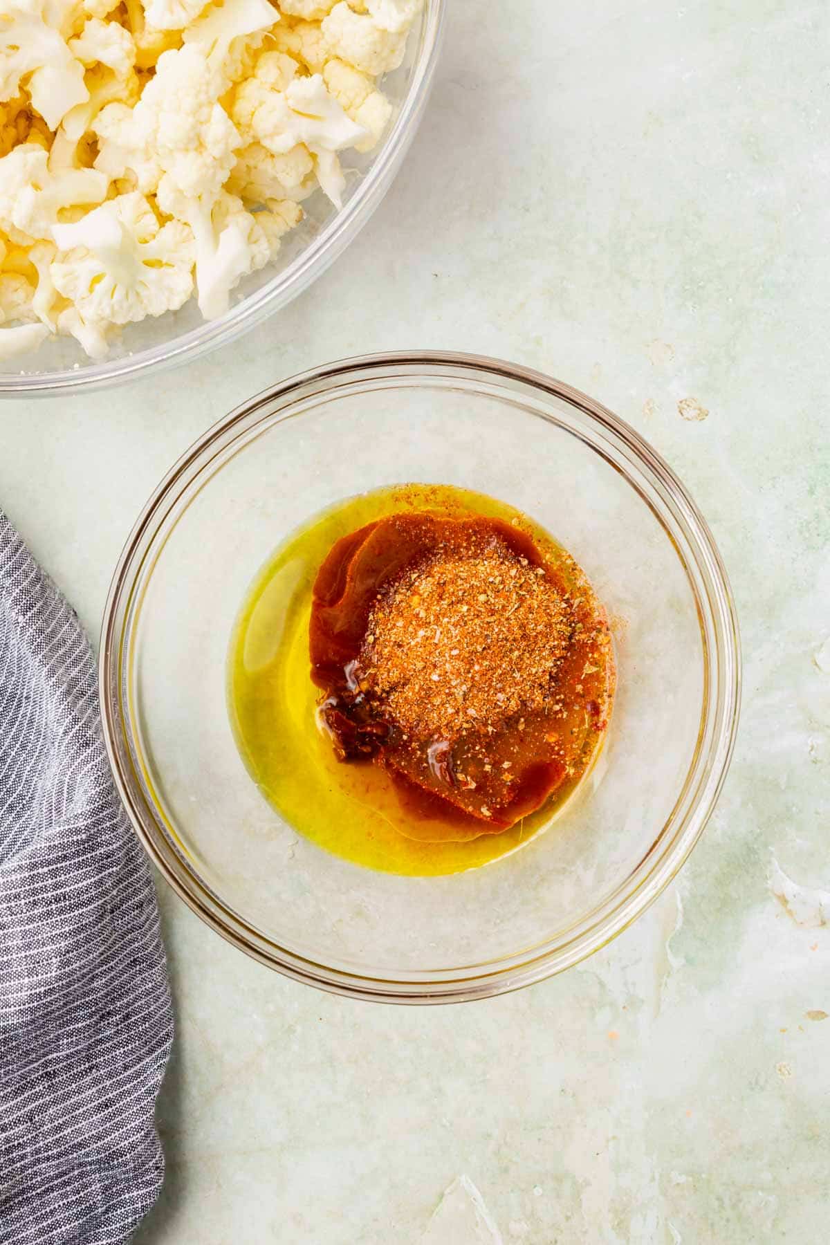 A small glass mixing bowl with olive oil, adobo sauce, chopped chipotle peppers in adobo sauce, and taco seasoning before mixing.