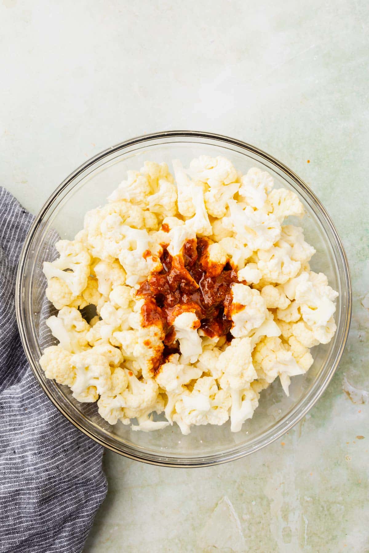 Cauliflower florets in a glass mixing bowl topped with an adobo sauce mixture before mixing.
