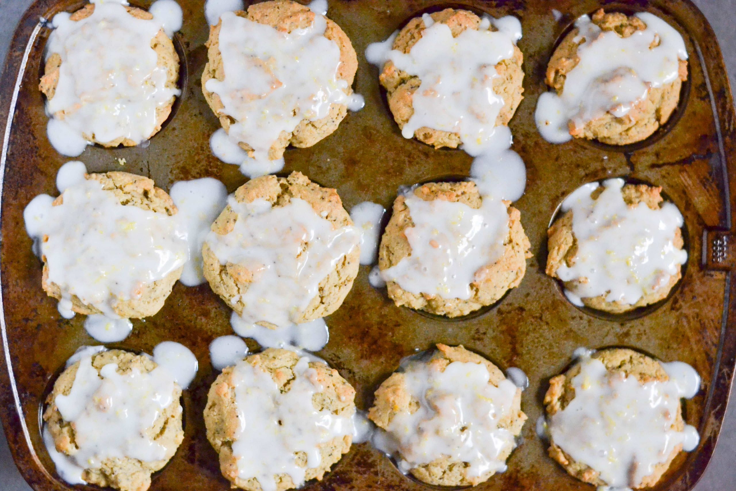 An overhead view of a muffin tin with lemon poppyseed muffins with glaze.