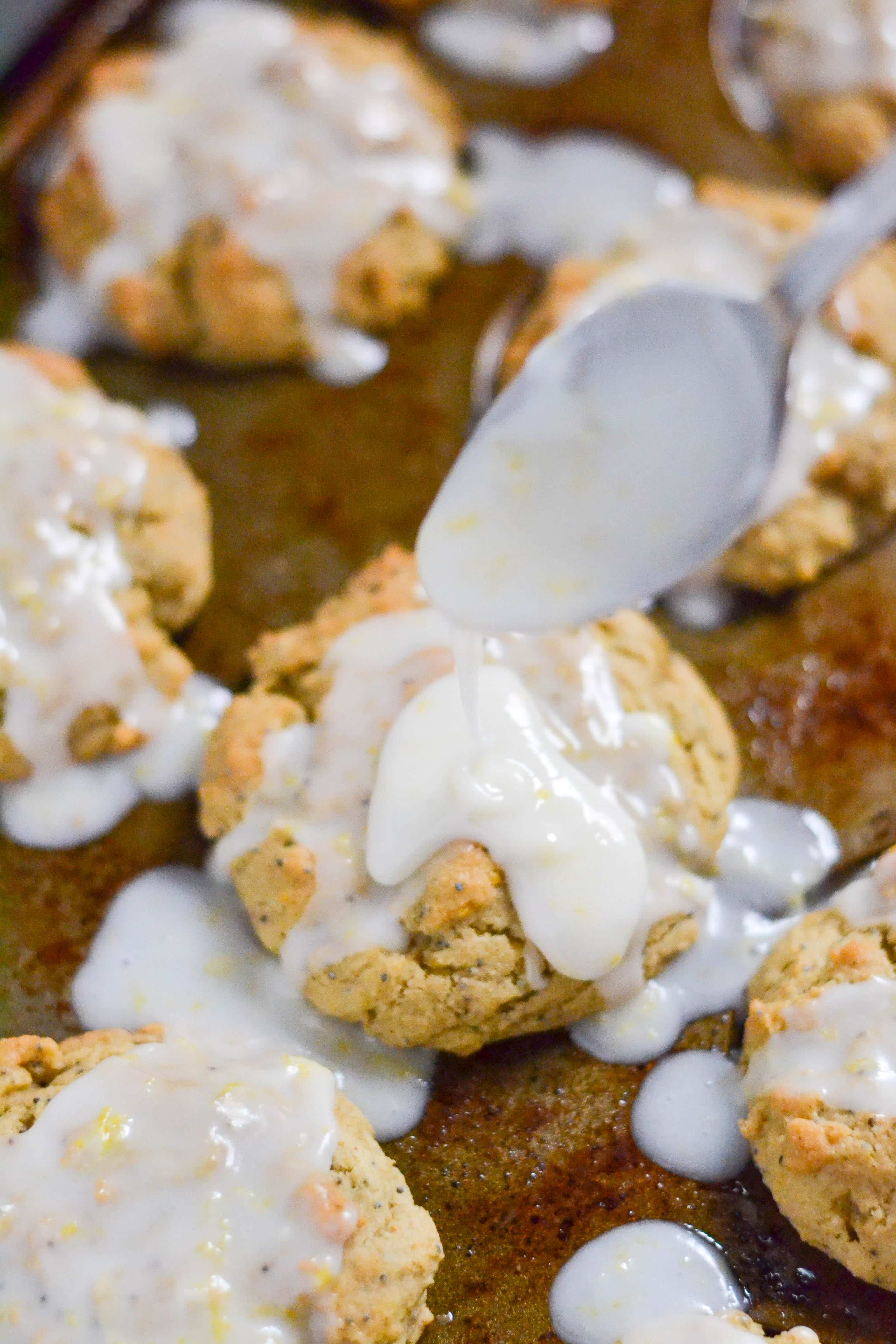 A spoon pouring glaze on a lemon poppyseed muffin in a muffin tin.