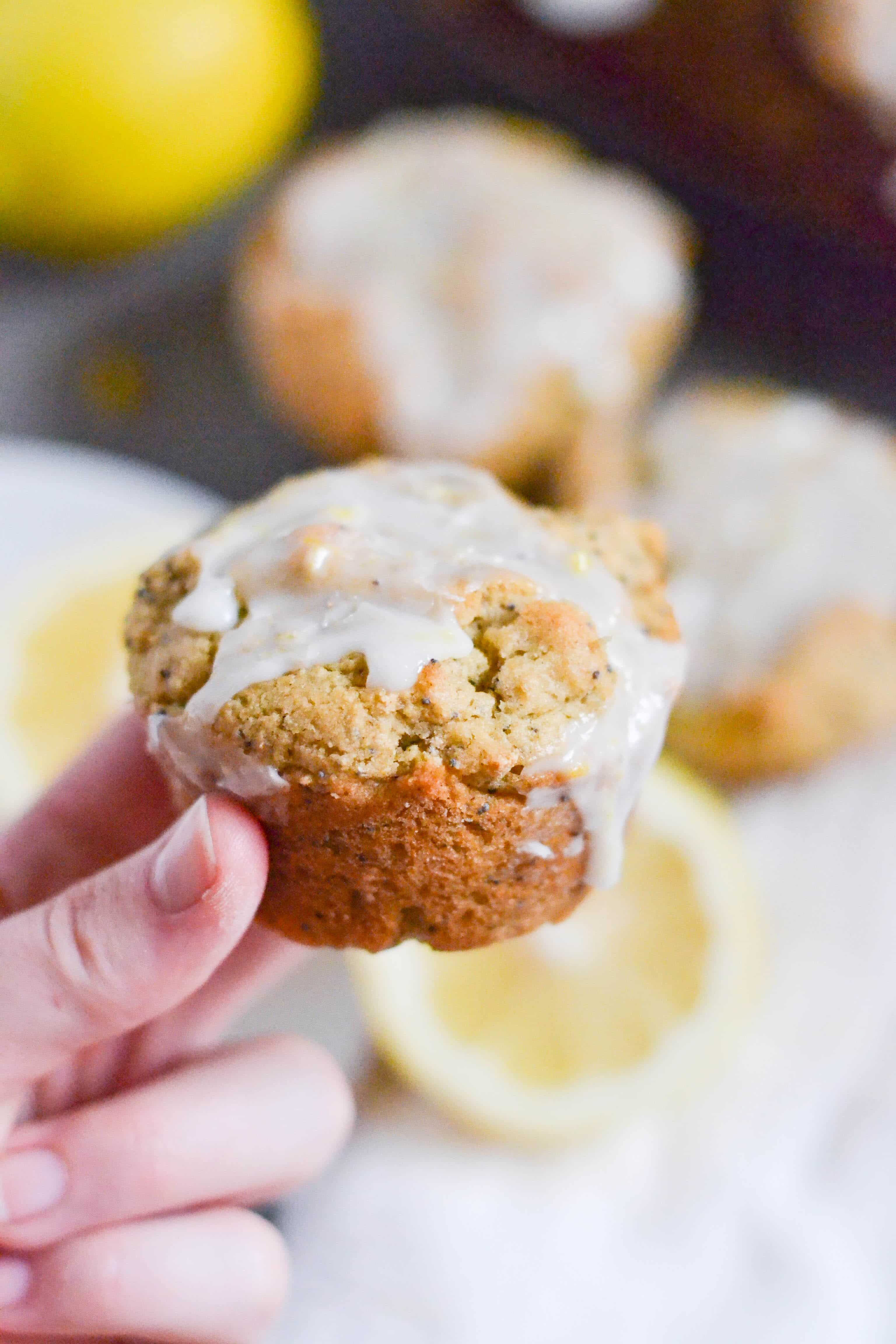 A hand holding a vegan gluten-free lemon poppyseed muffin with lemon glaze on it.