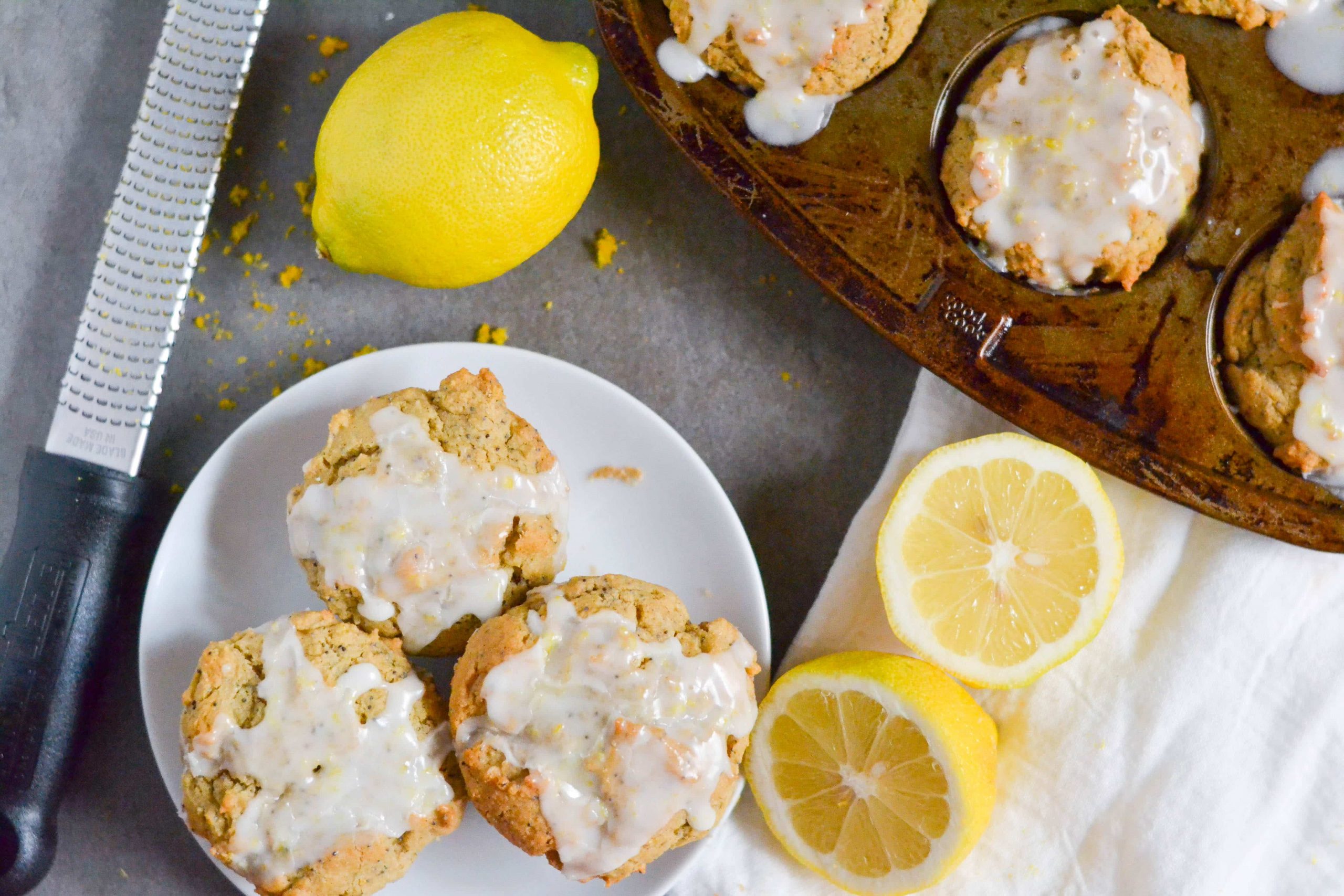 A muffin pan with lemon poppyseed muffins in it with a plate next to it with three poppyseed muffins on it.