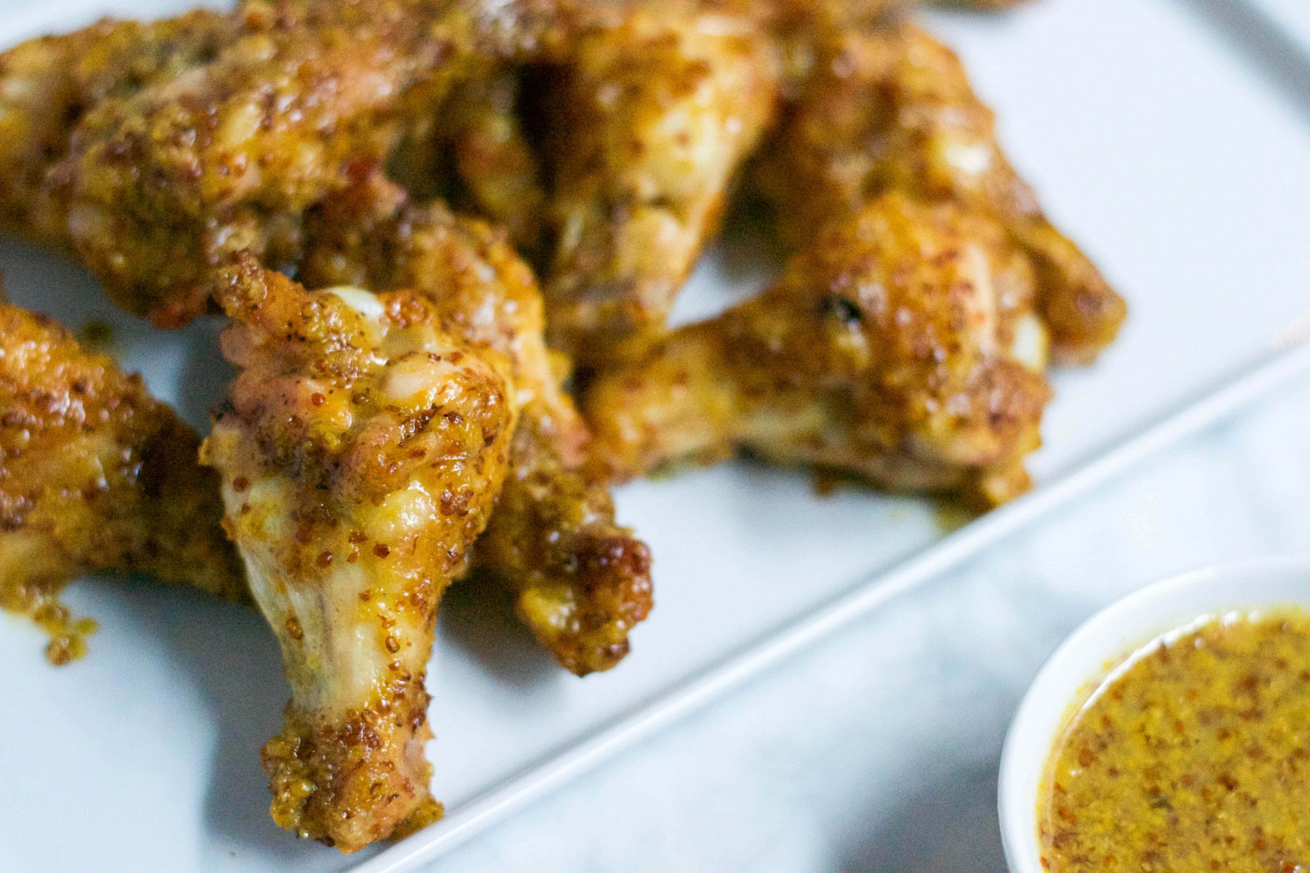 Close-up of Honey Mustard Baked Chicken Wings on a white plate, served alongside a small bowl of grainy mustard dipping sauce.