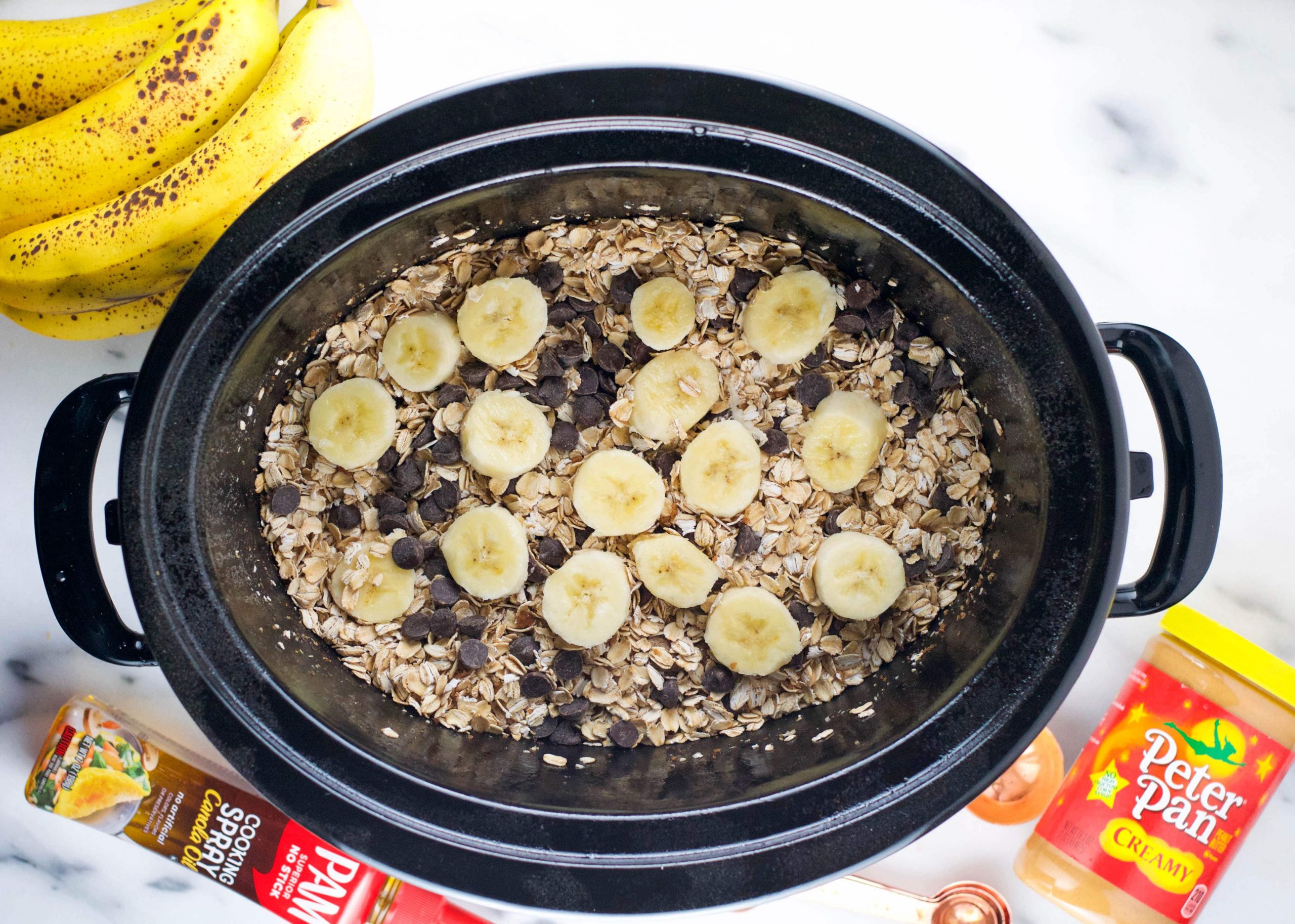 A slow cooker with oats, chocolate chips, and banana in it before cooking.