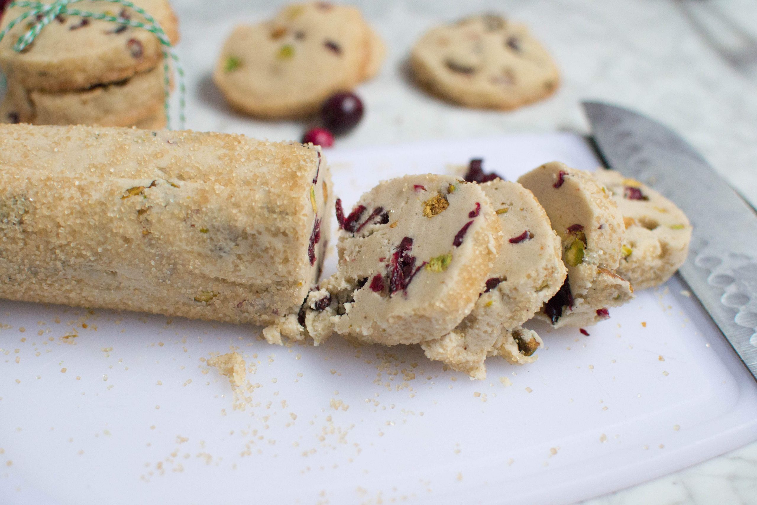 A log of raw cranberry pistachio cookie dough that has three slices cut off from it.