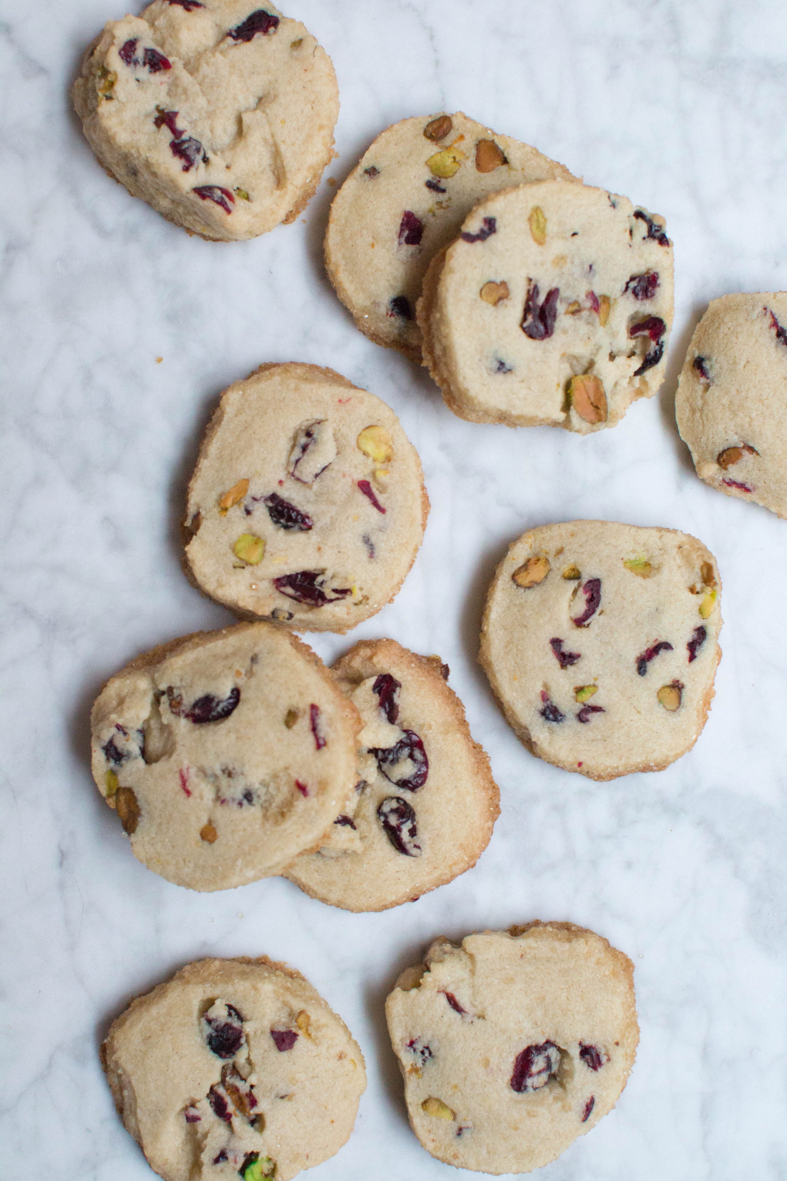 Cranberry pistachio shortbread cookies scattered on a marble surface.