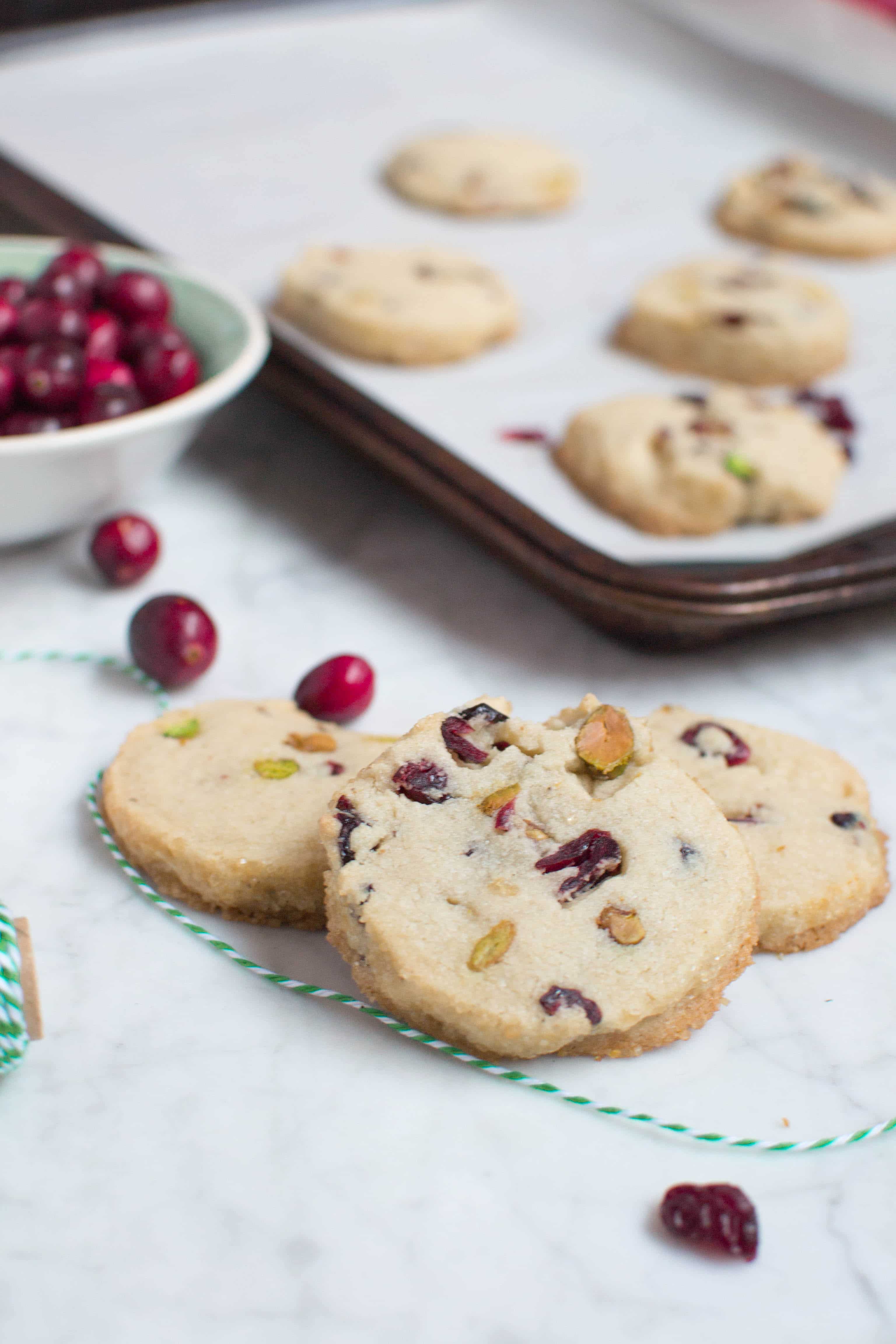 Three cranberry pistachio cookies layered on top of each other with a baking sheet in the background.