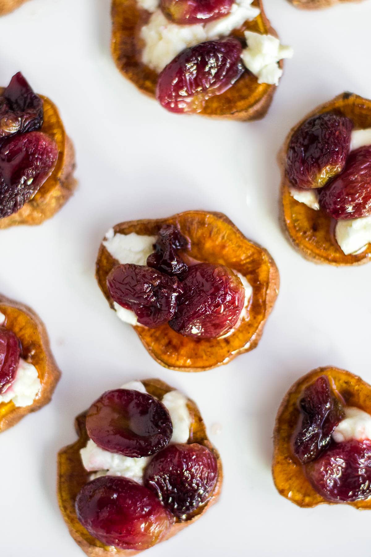 An aerial view of sweet potato rounds, roasted grapes with goat cheese on a white platter.