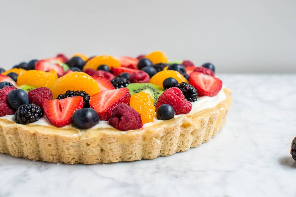 A straight on view of a shortbread crusted gluten-free fruit tart with berries, oranges, and kiwi.