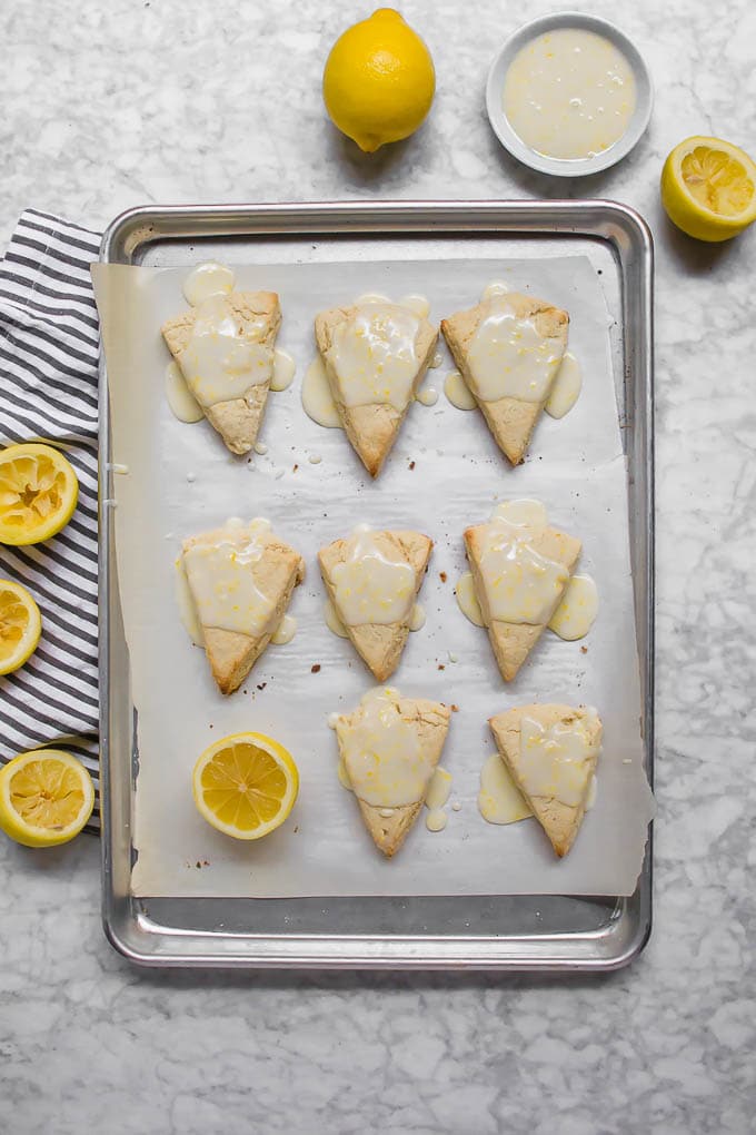 An aerial view of a baking sheet with white parchment paper with 8 lemon scones and a lemon half.