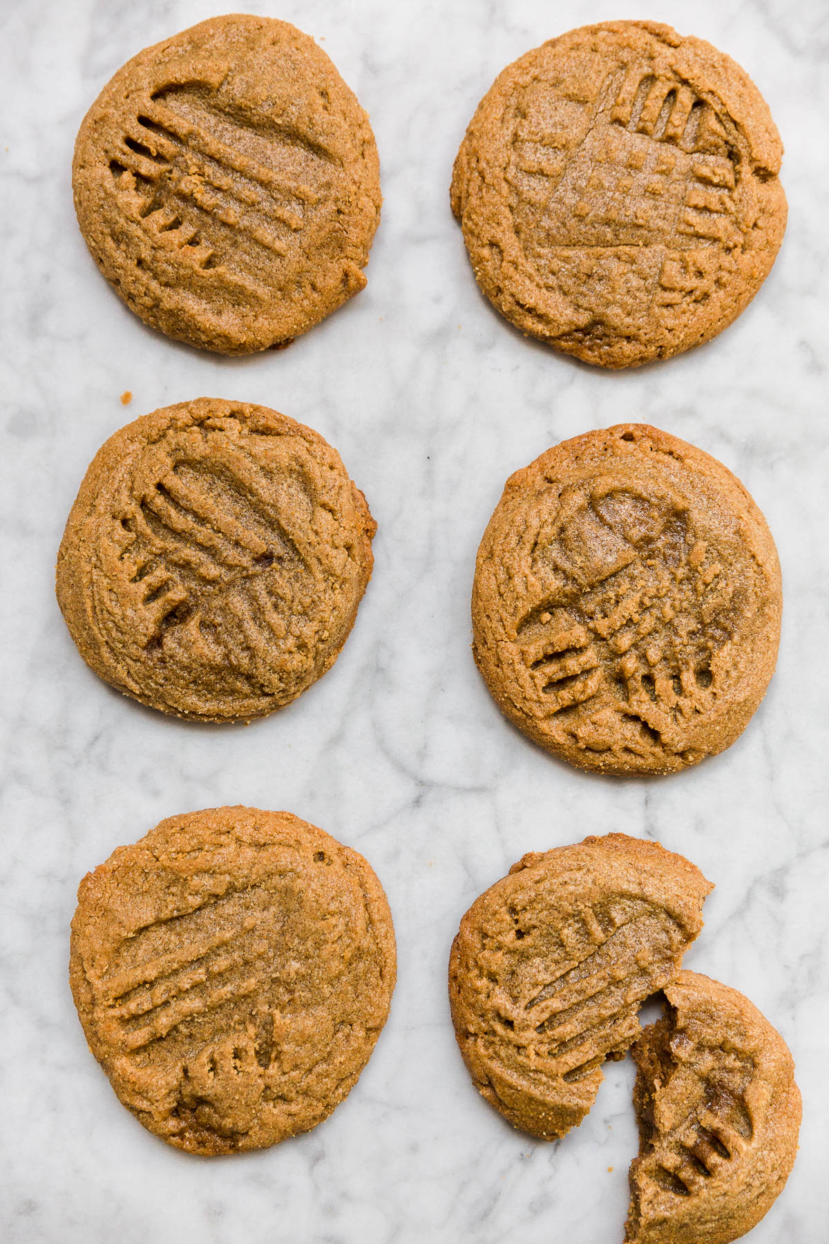 Aerial view of flourless peanut butter cookies in two rows with one cookie broken.