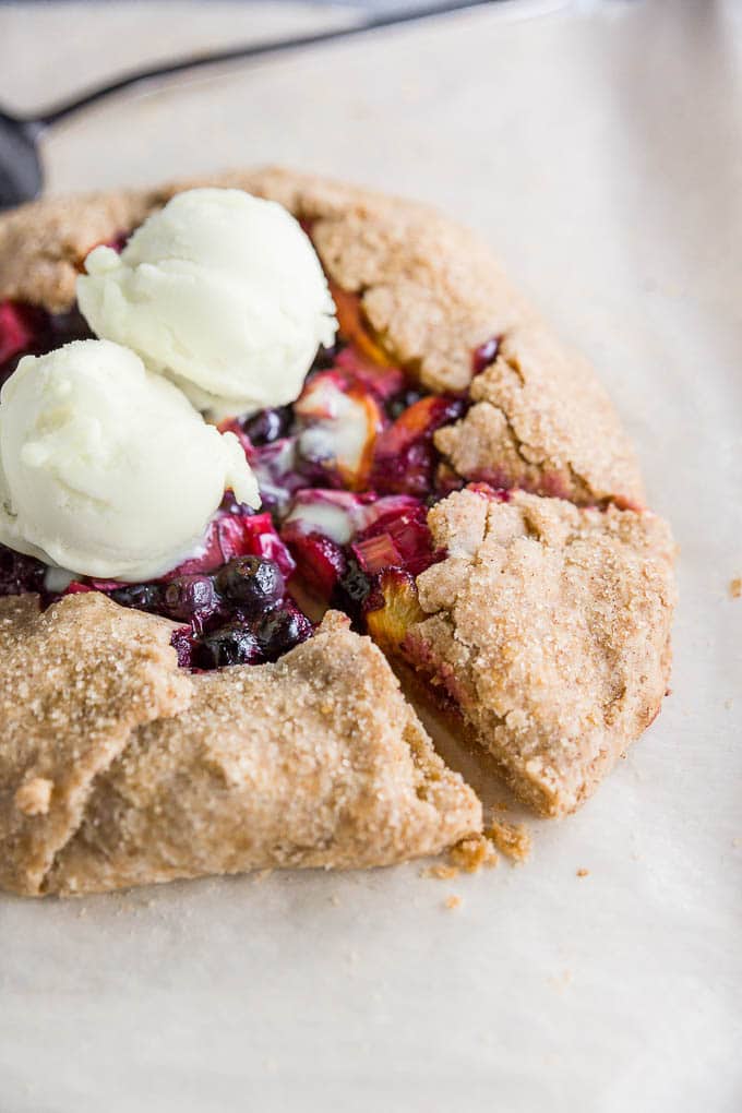 A straight on view of a gluten-free, vegan, dairy-free peach blueberry rhubarb galette with vanilla ice cream on top.