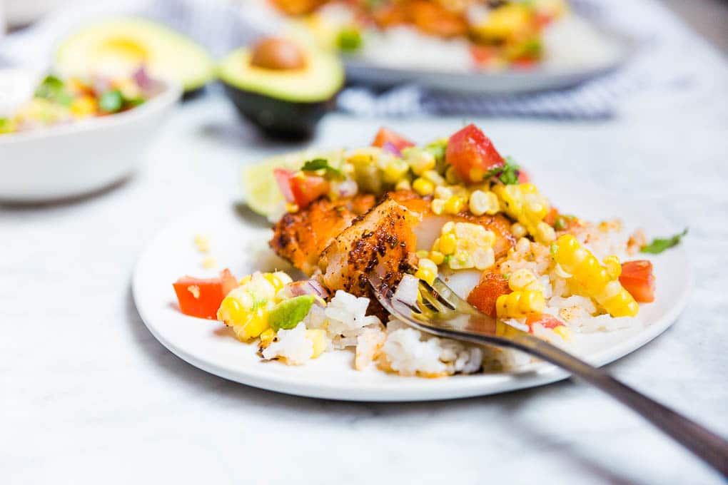 A plate of blackened cod with a fork and avocado tomato corn salsa.